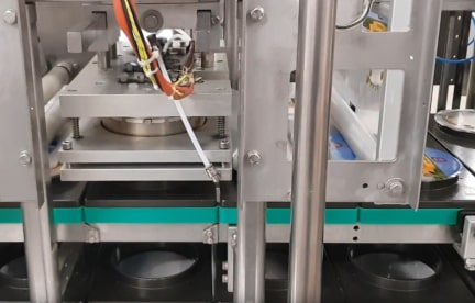 The lidding film heat seal sub-system of soft,  spoonable food processing machinery.